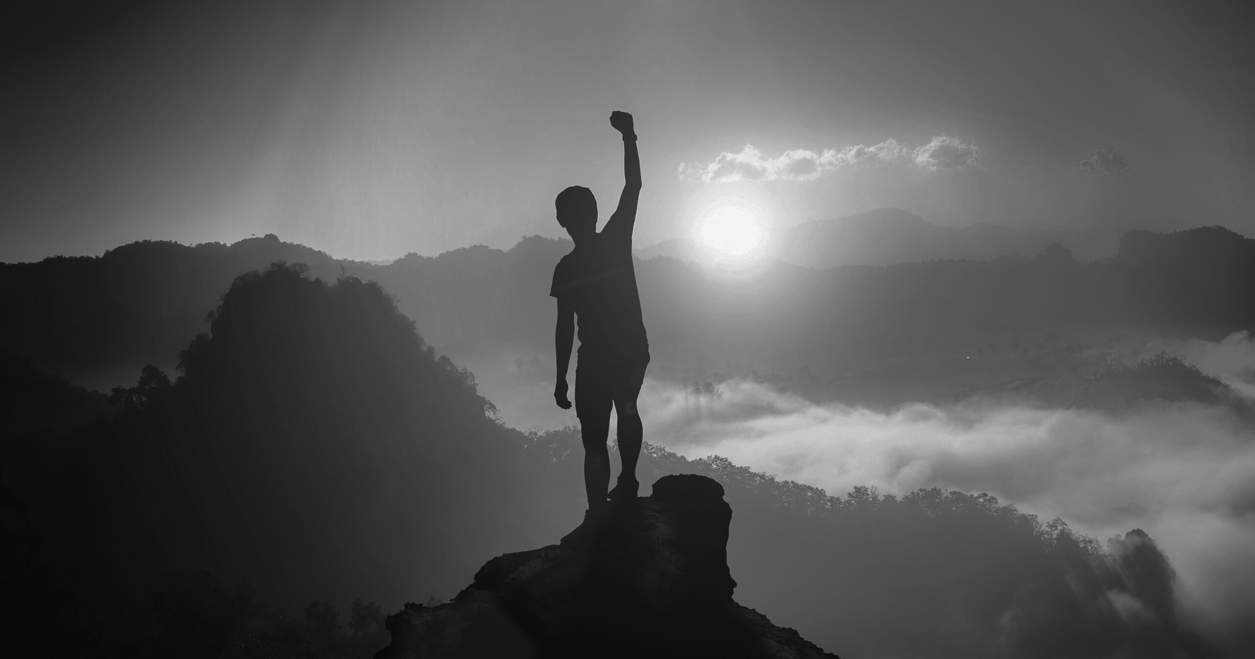 Silhouette of a man on top a of mountain peak with fist raised
